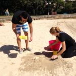 Two people engaged in a small business marketing workshop, mentoring each other while digging in the sand on a beach.