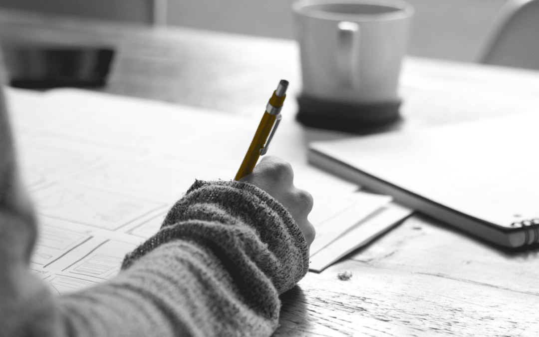 A person engaged in a small business marketing workshop, diligently writing with a pen at a desk while receiving mentoring.