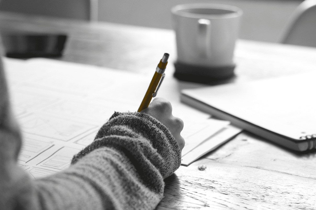 A person engaged in a small business marketing workshop, diligently writing with a pen at a desk while receiving mentoring.