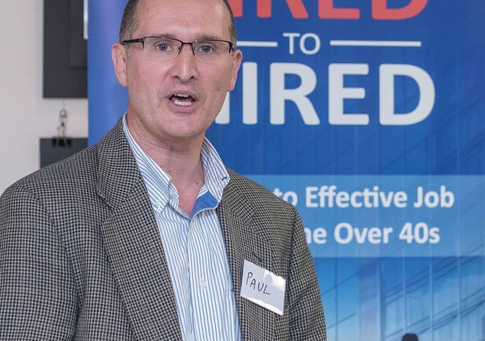 A man standing in front of a banner that says "fired to hired" at a marketing workshop.