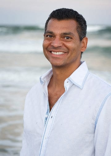 A man in a white shirt standing on the beach, seeking mentorship in small business marketing.