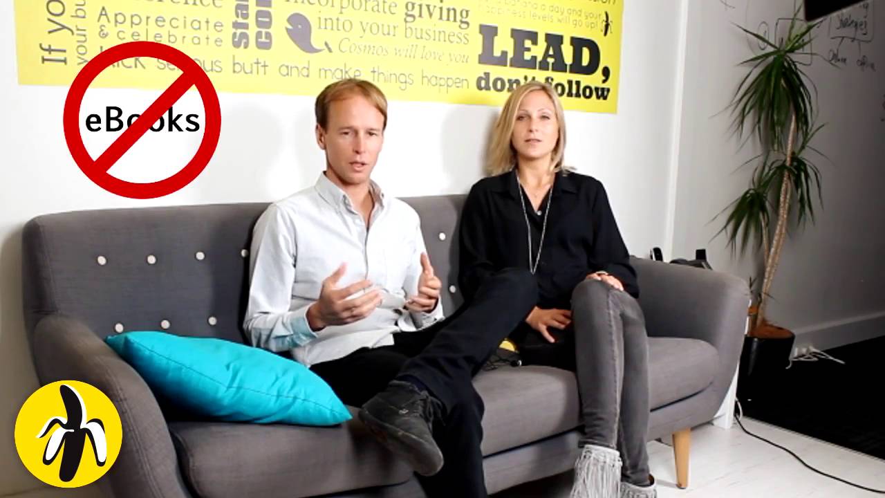 Two people sitting on a couch in front of a yellow sign during a marketing workshop.