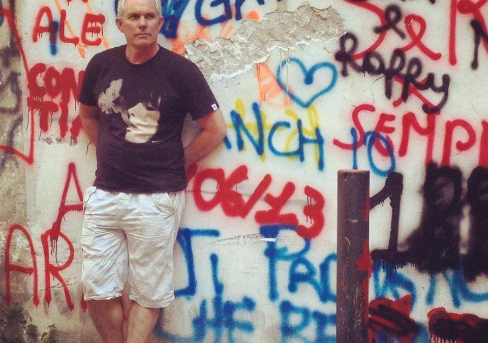 A man standing in front of a wall covered in graffiti, contemplating his small business marketing strategy.