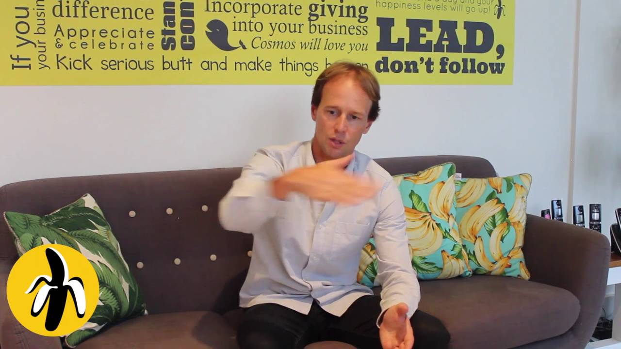 A man sitting on a couch participating in a marketing workshop and mentoring session, with a yellow wall serving as the backdrop.