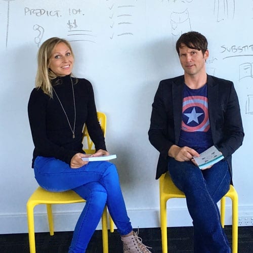 Two people participating in a marketing workshop, sitting on yellow chairs and writing on a white board.