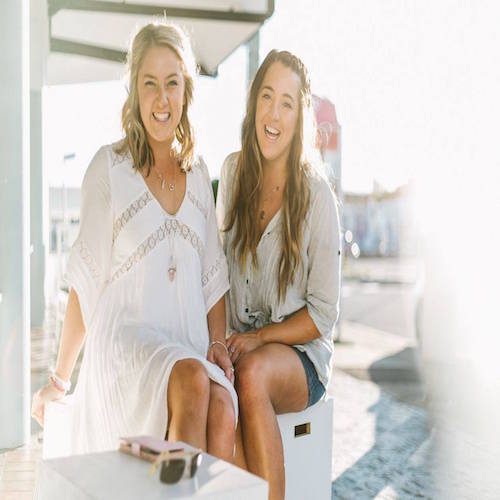 Two women participating in a small business marketing mentoring session while sitting on a bench in front of a store.