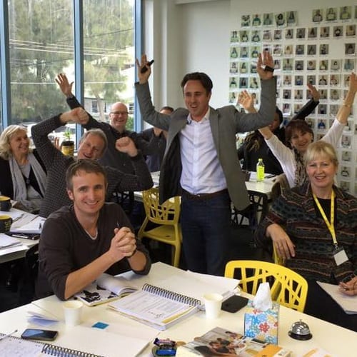 A group attending a marketing workshop with their hands raised.