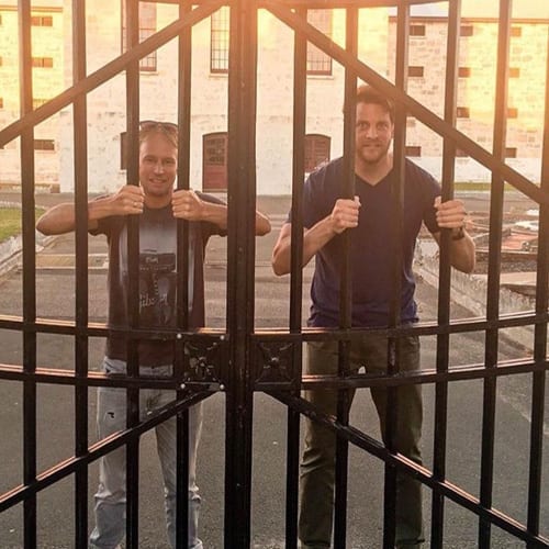 Two men participating in a marketing workshop while standing in front of an iron gate.