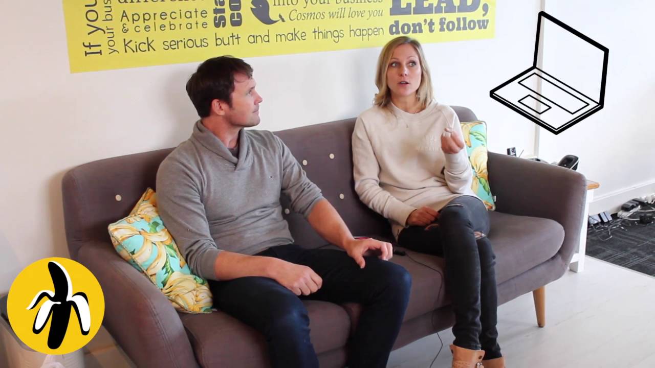 A man and woman participating in a small business marketing workshop, sitting on a couch in front of a yellow wall.