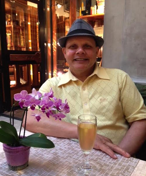 A man in a hat sitting at a table with a glass of wine, attending a small business marketing workshop for mentoring.