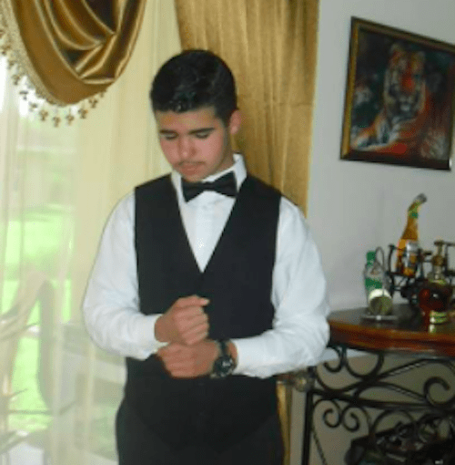 A young man in a tuxedo standing in front of a window, providing mentoring for small business marketing during a marketing workshop.