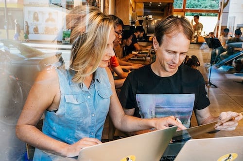 Two people participating in a marketing workshop while working on laptops in a cafe.