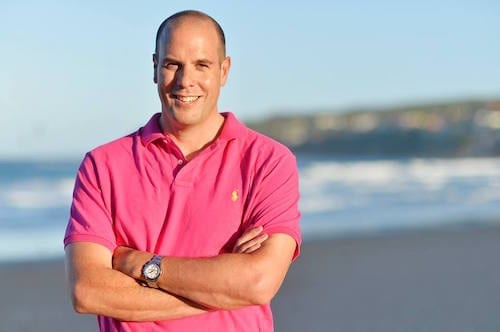 A man in a pink shirt standing on the beach, participating in a marketing workshop.