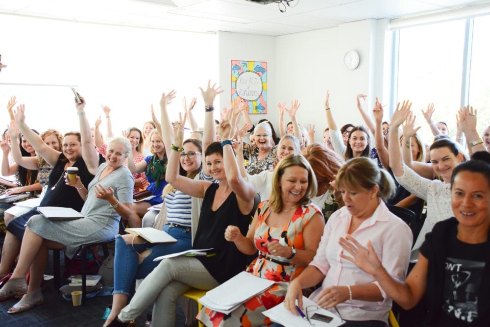 A marketing workshop where a group of people in a classroom are raising their hands to participate in discussions about small business marketing.