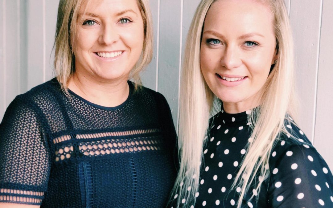 Two women posing for a photo during a marketing workshop in front of a white wall.