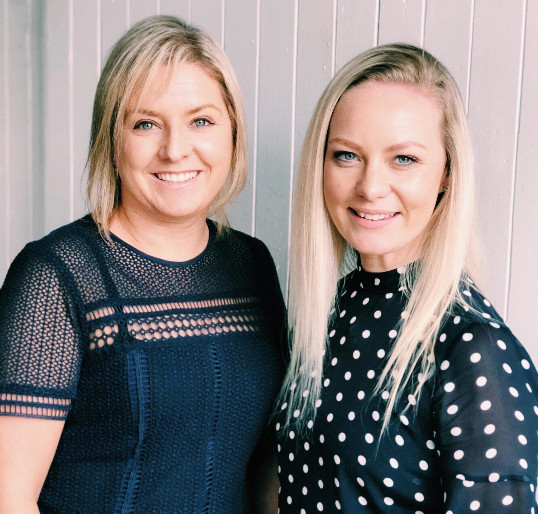 Two women posing for a photo during a marketing workshop in front of a white wall.
