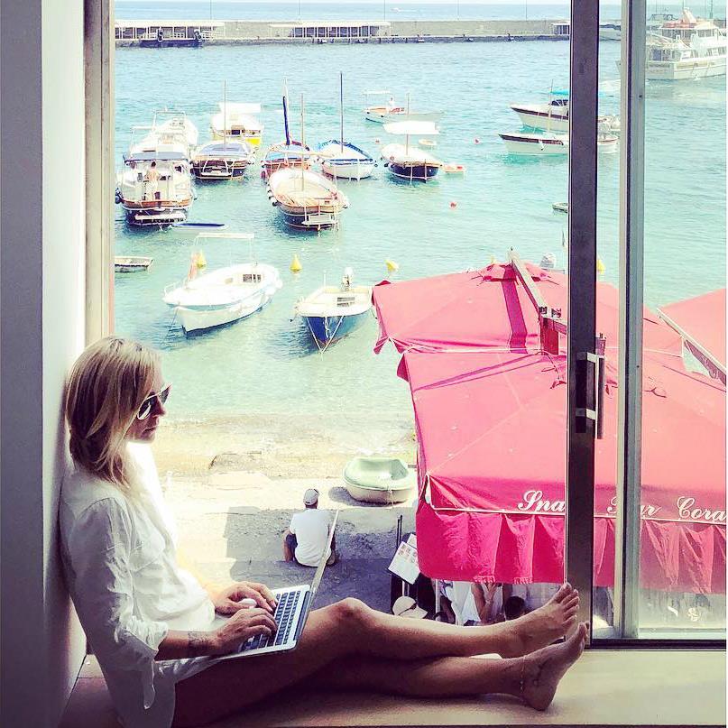 A woman participating in a marketing workshop, sitting on a window sill with a laptop.