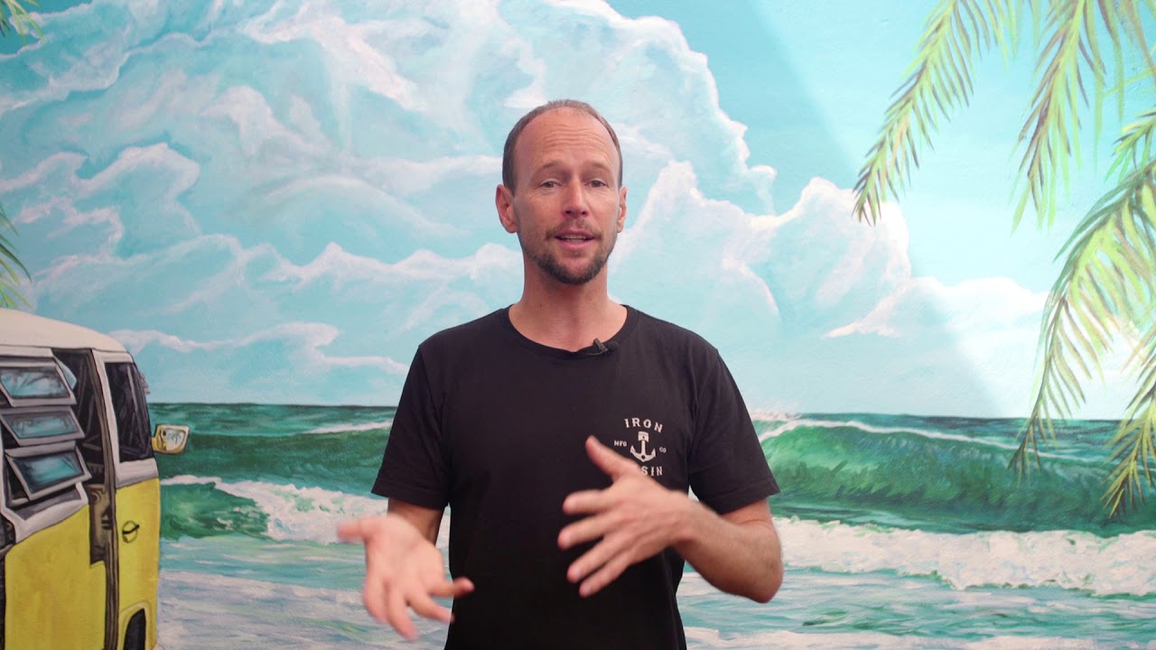 A man standing in front of a mural with palm trees and a VW bus during a marketing workshop.