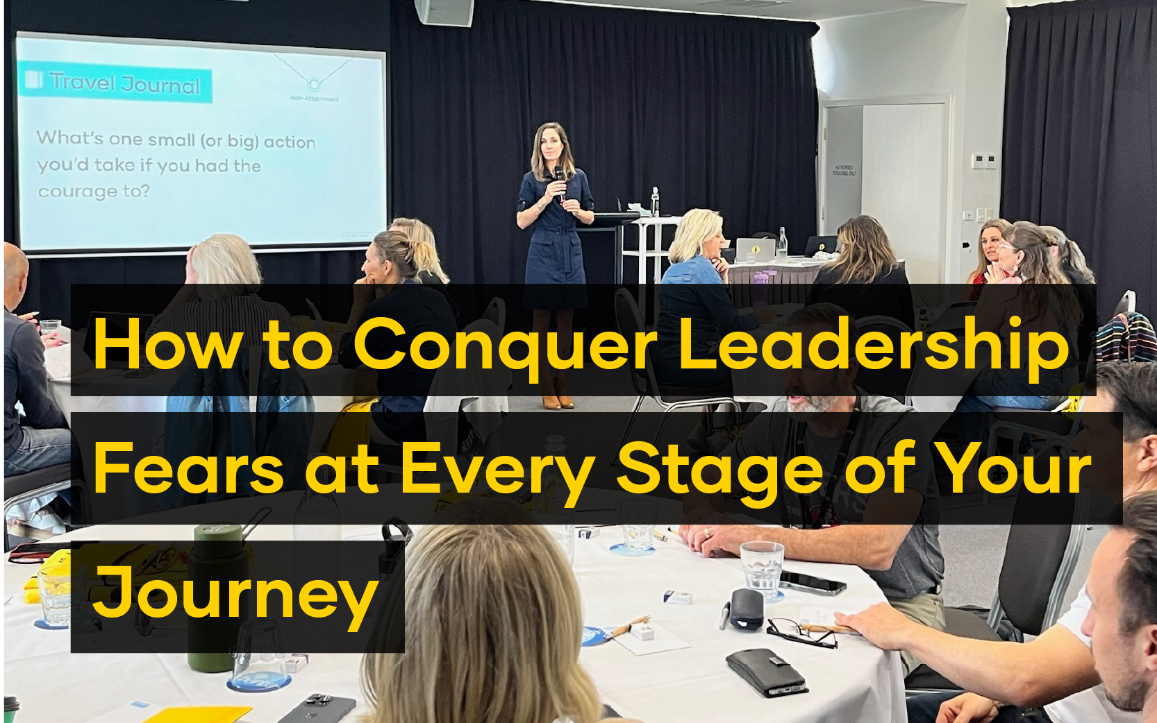A woman addresses a seated audience in a conference room, presenting a slide that asks, "What's one small (or big) action you'd take if you had the courage to?"—inviting them to confront their leadership fears.