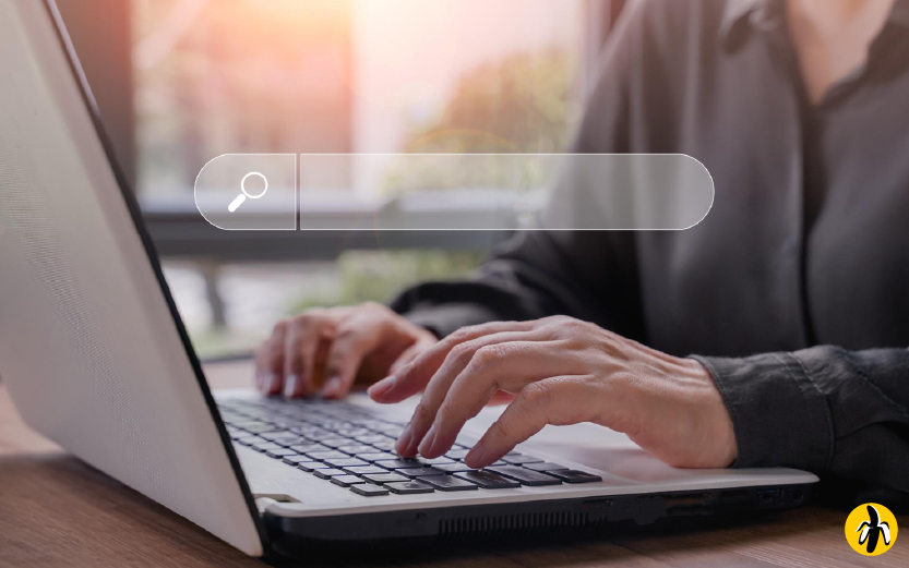 Person typing on a laptop with a translucent search bar graphic overlay, suggesting a search action.